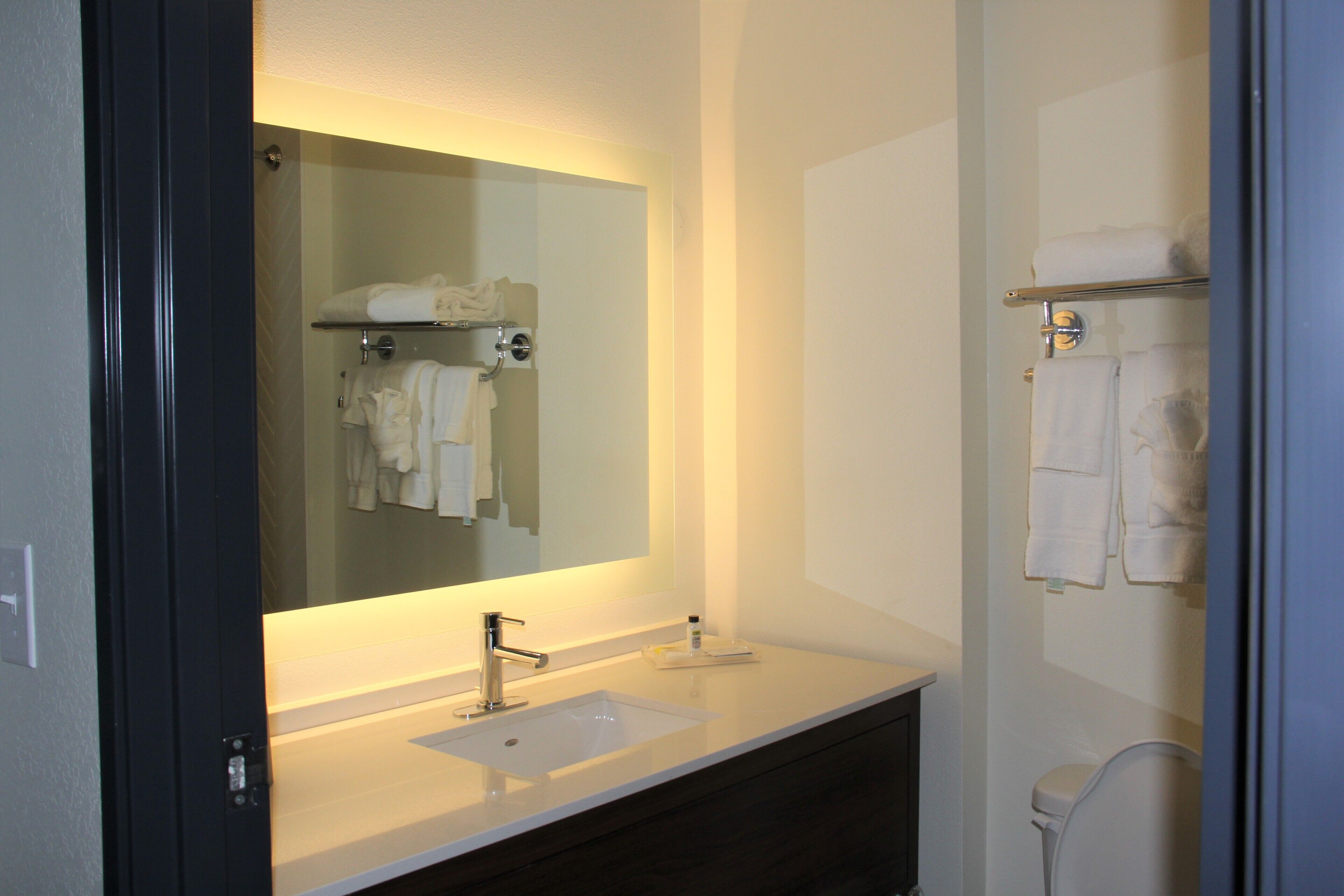 A modern bathroom with a large mirror, a white sink, and a dark vanity.