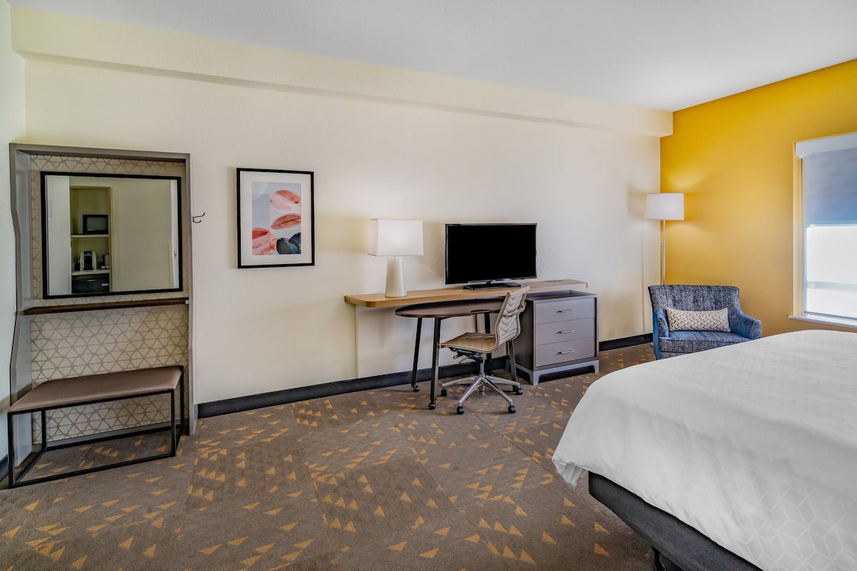 A hotel room with a bed, desk, chair, TV, and a small bench.