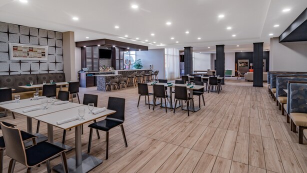 A spacious dining area with multiple tables and chairs, a bar area, and a seating section with cushioned benches. - Holiday Inn Southaven Central - Memphis by IHG (Southaven)