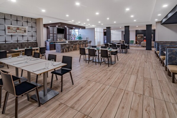 Un'ampia sala da pranzo con diversi tavoli e sedie, un angolo bar e una zona relax con panche imbottite.
