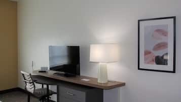 Ein Hotelzimmer mit Schreibtisch, Fernseher, Lampe, Stuhl und einem gerahmten Bild an der Wand.