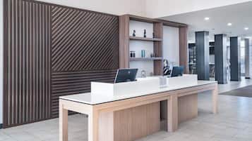 A reception desk with a computer, a wooden panel wall, and a shelving unit with decorative items.