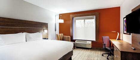 A hotel room with a large bed, a desk, a chair, a TV, and a window with blinds.