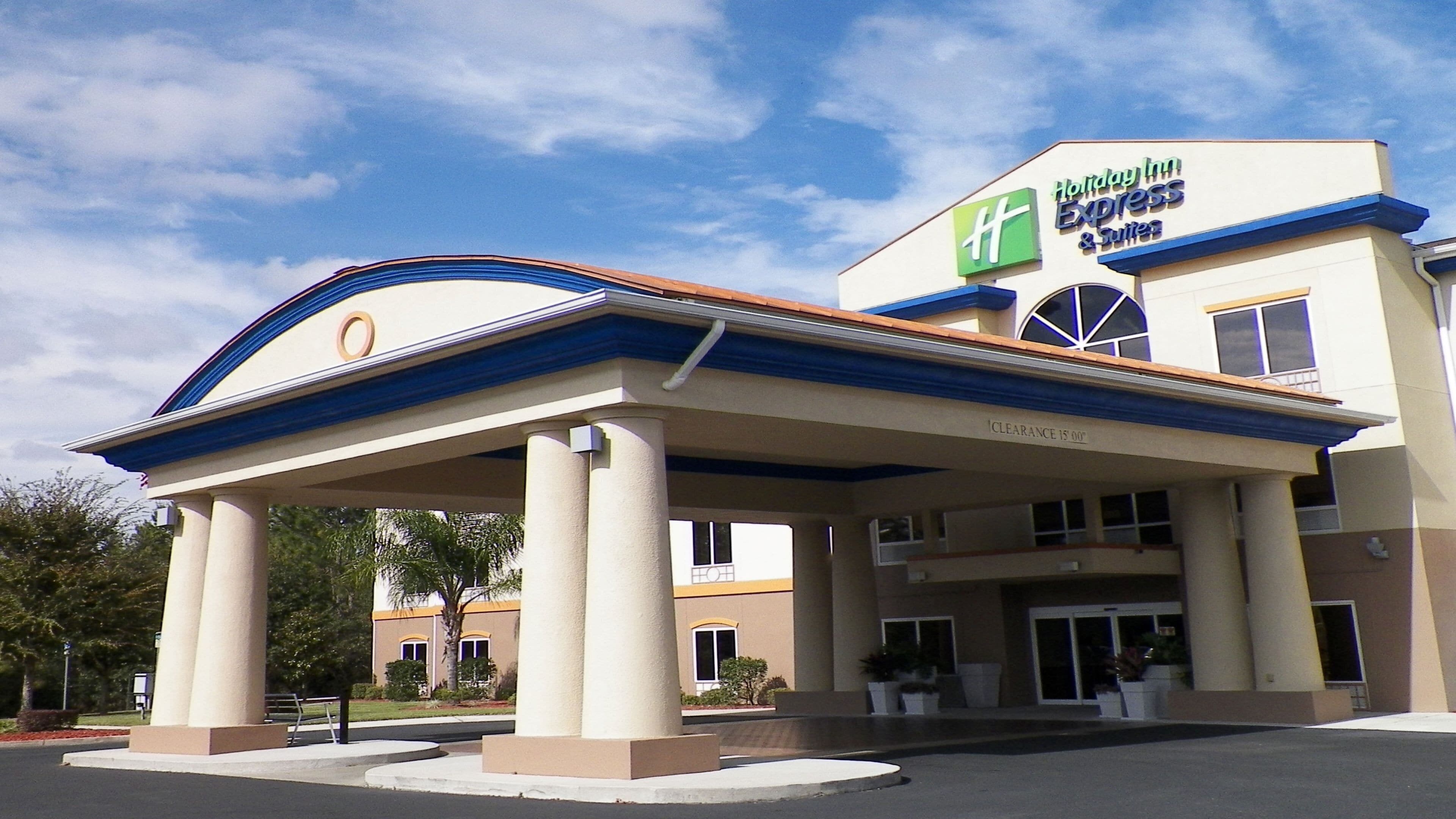 Edificio de Holiday Inn Express & Suites con entrada cubierta, columnas y cielo despejado.