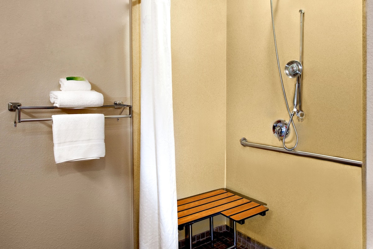 Une salle de bain avec une douche, un porte-serviettes avec des serviettes et un petit banc en bois.