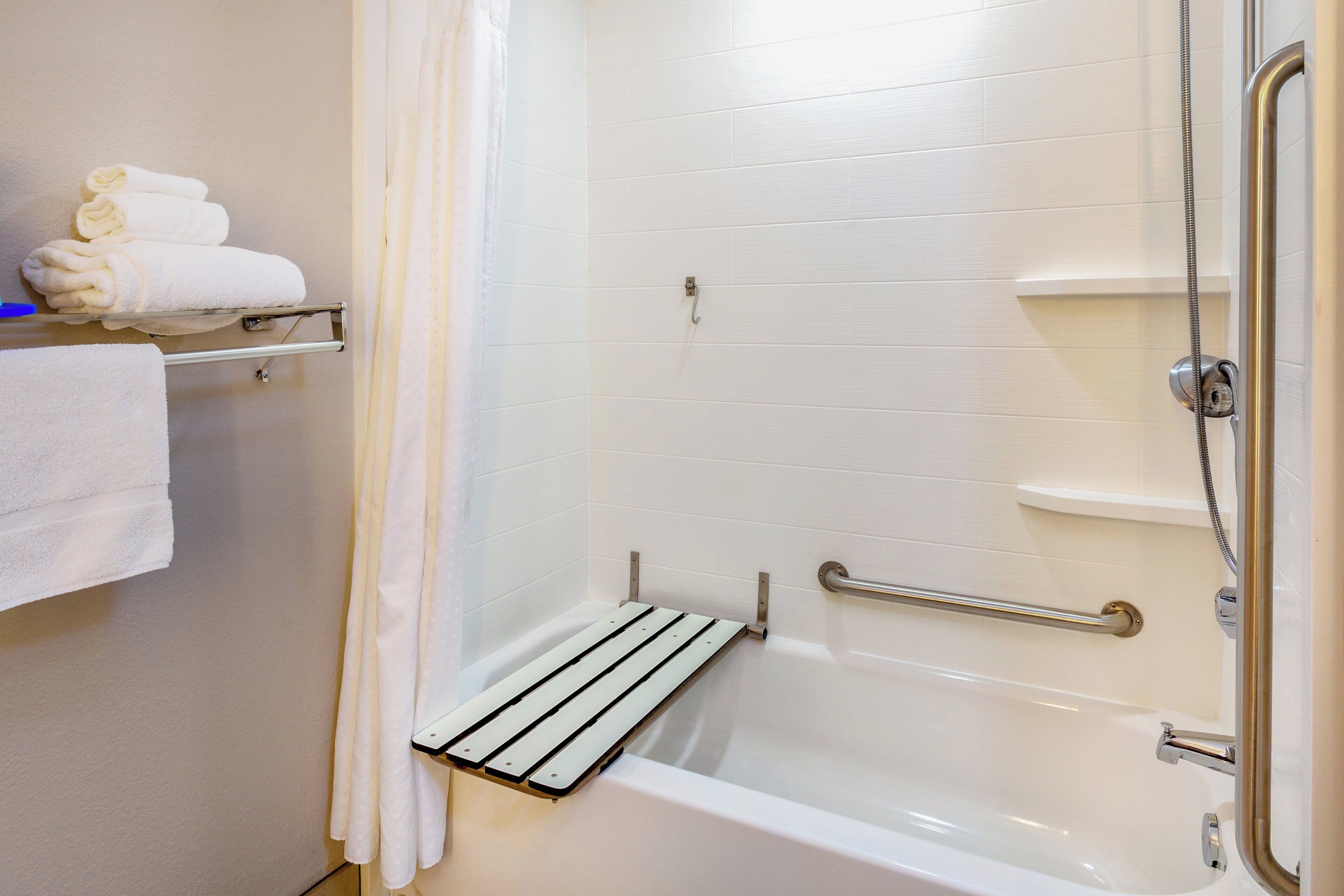 A bathroom with a white bathtub, a shower with a handheld showerhead, a towel rack with folded towels, and a grab bar for safety.