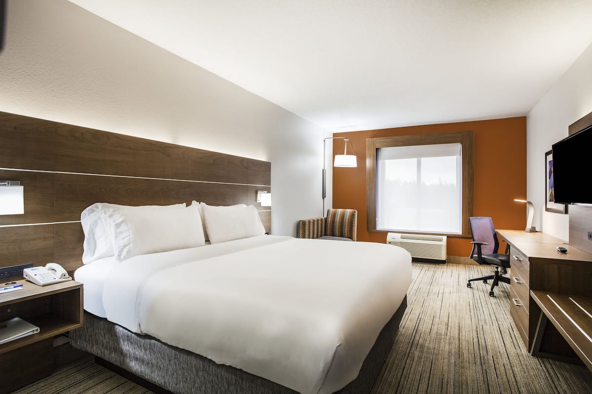 Une chambre d’hôtel avec un grand lit, un bureau avec un ordinateur, une chaise, une télévision et une fenêtre donnant sur un beau paysage.
