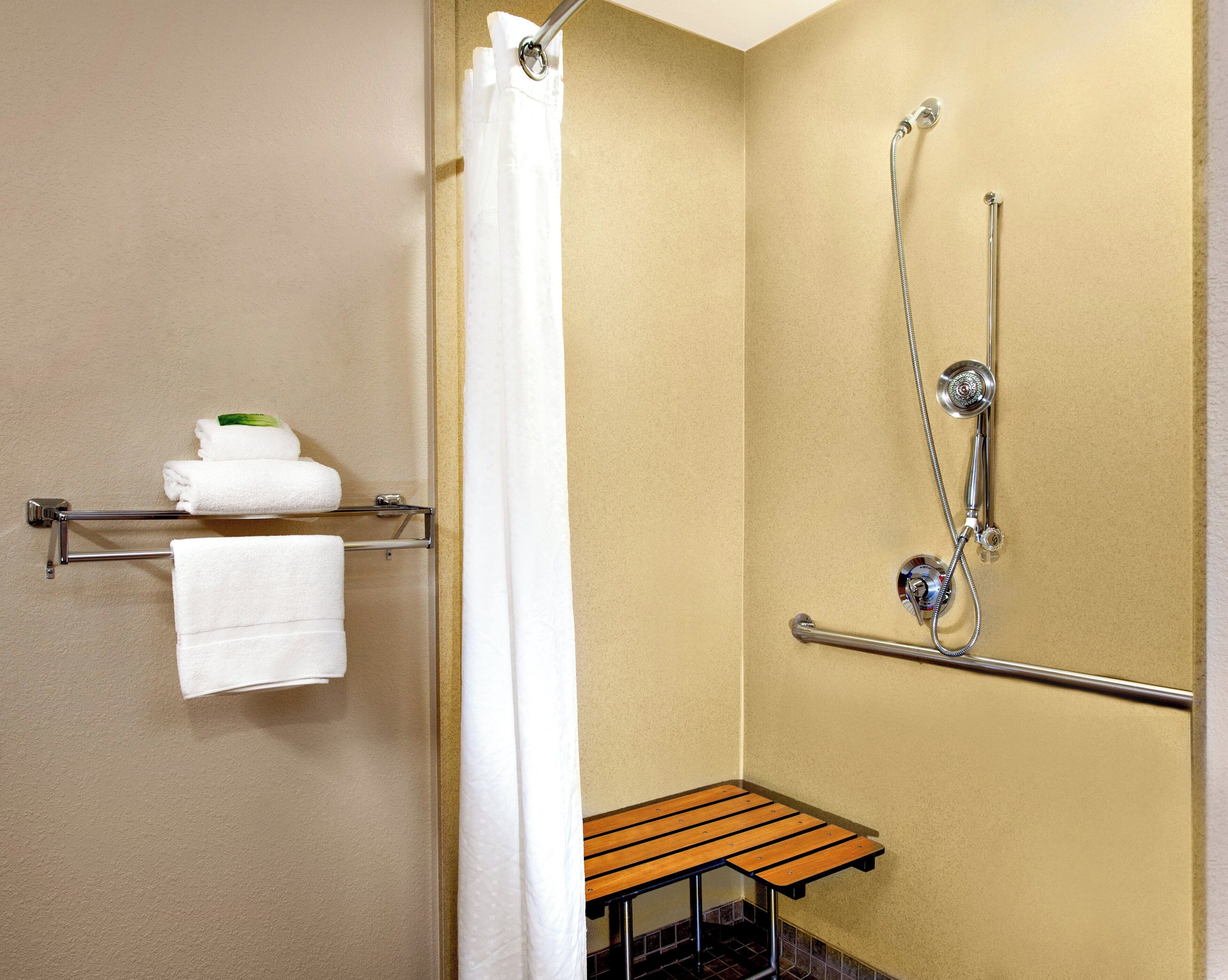 A shower area with a grab bar, a towel rack with towels, and a small wooden bench.
