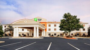 A Holiday Inn Express & Suites with a central entrance, parking lot, and surrounding greenery.