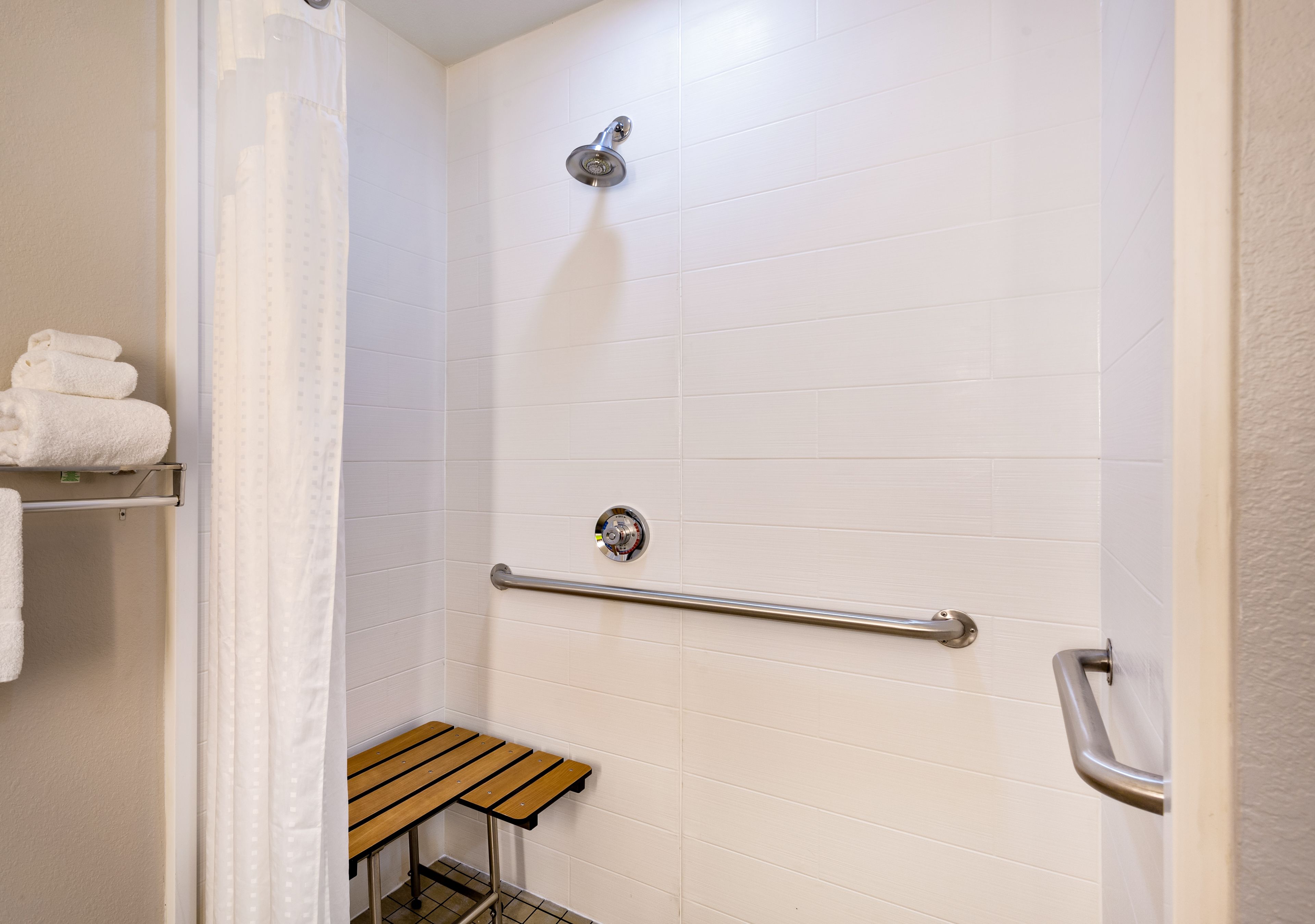 A shower area with white tiled walls, a showerhead, a grab bar, and a bench.