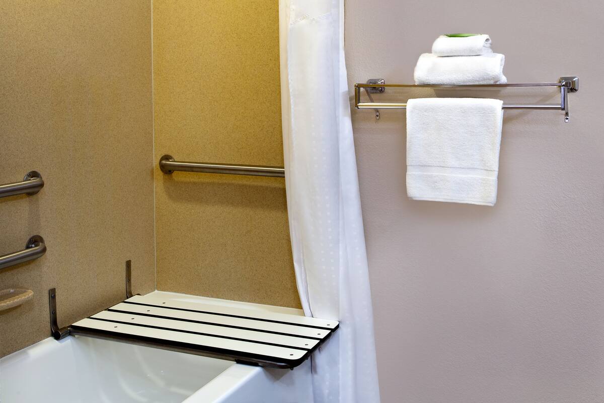 Une salle de bain équipée d’une baignoire, d’un rideau de douche, d’un porte-serviettes avec deux serviettes et d’une barre d’appui.