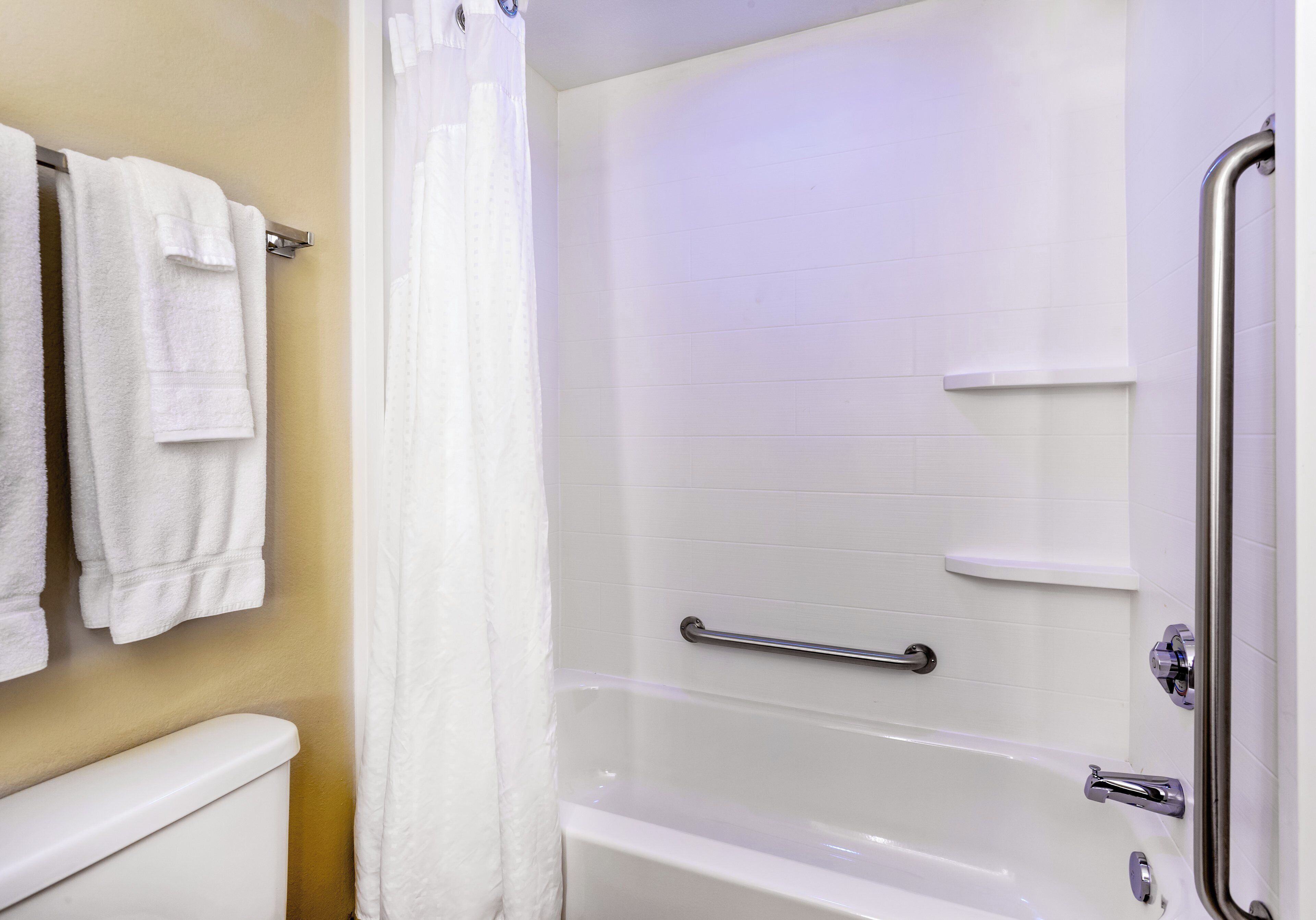 A bathroom with a white bathtub, a shower curtain, and a grab bar.