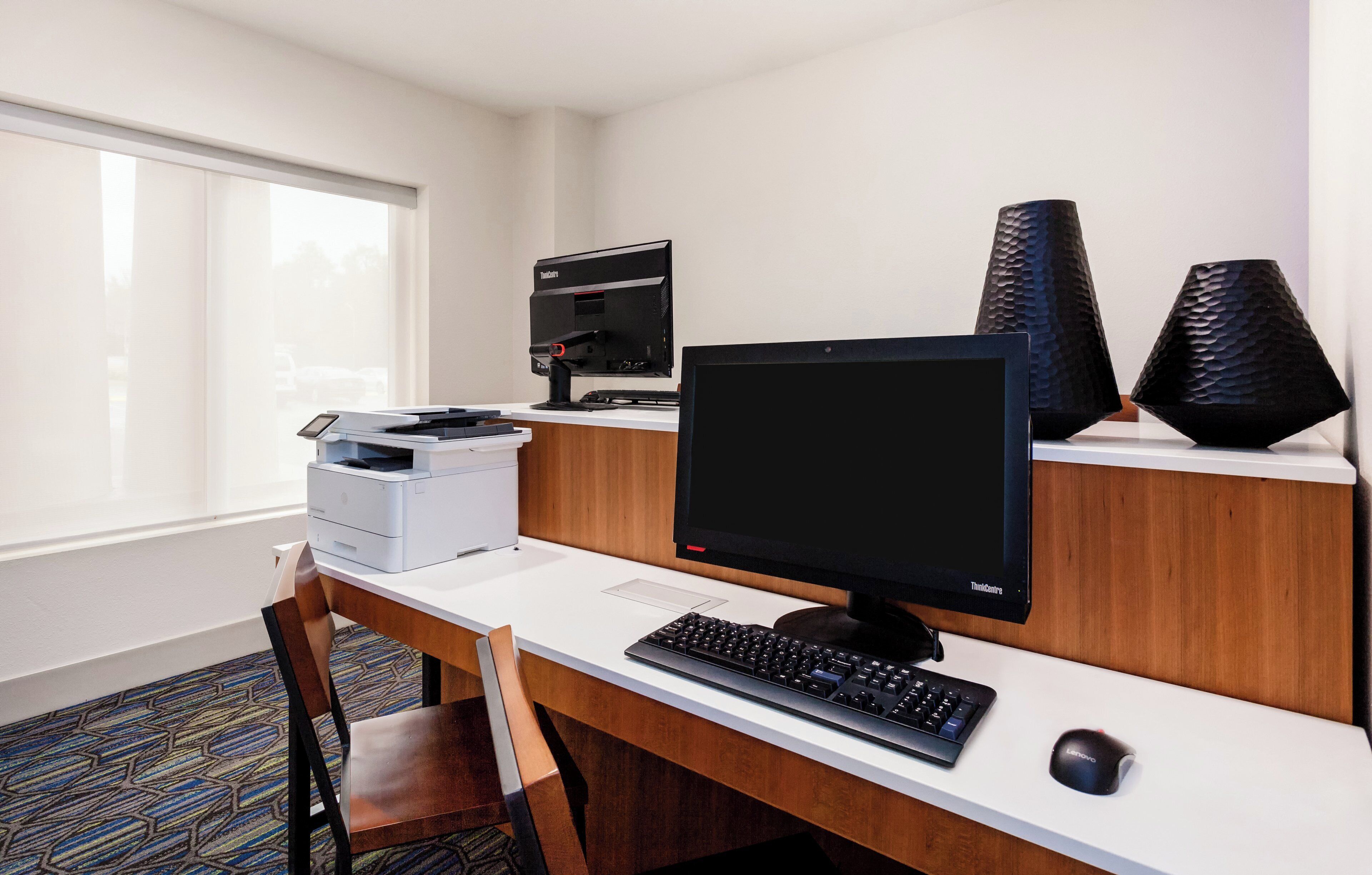 Una oficina de hotel con un escritorio, computadora, impresora y dos jarrones decorativos.