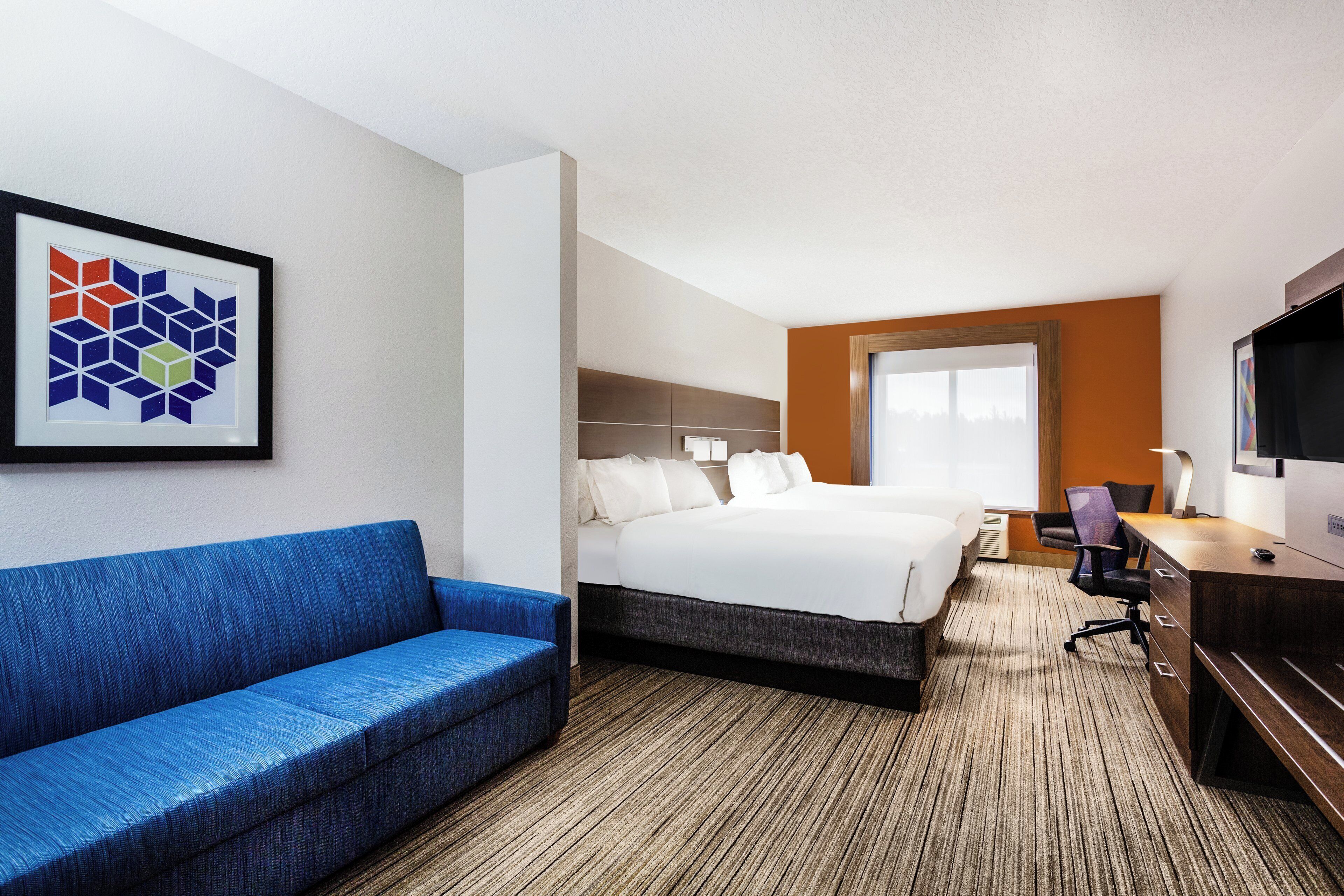 A hotel room with a bed, a blue sofa, a desk with a chair, and a television.