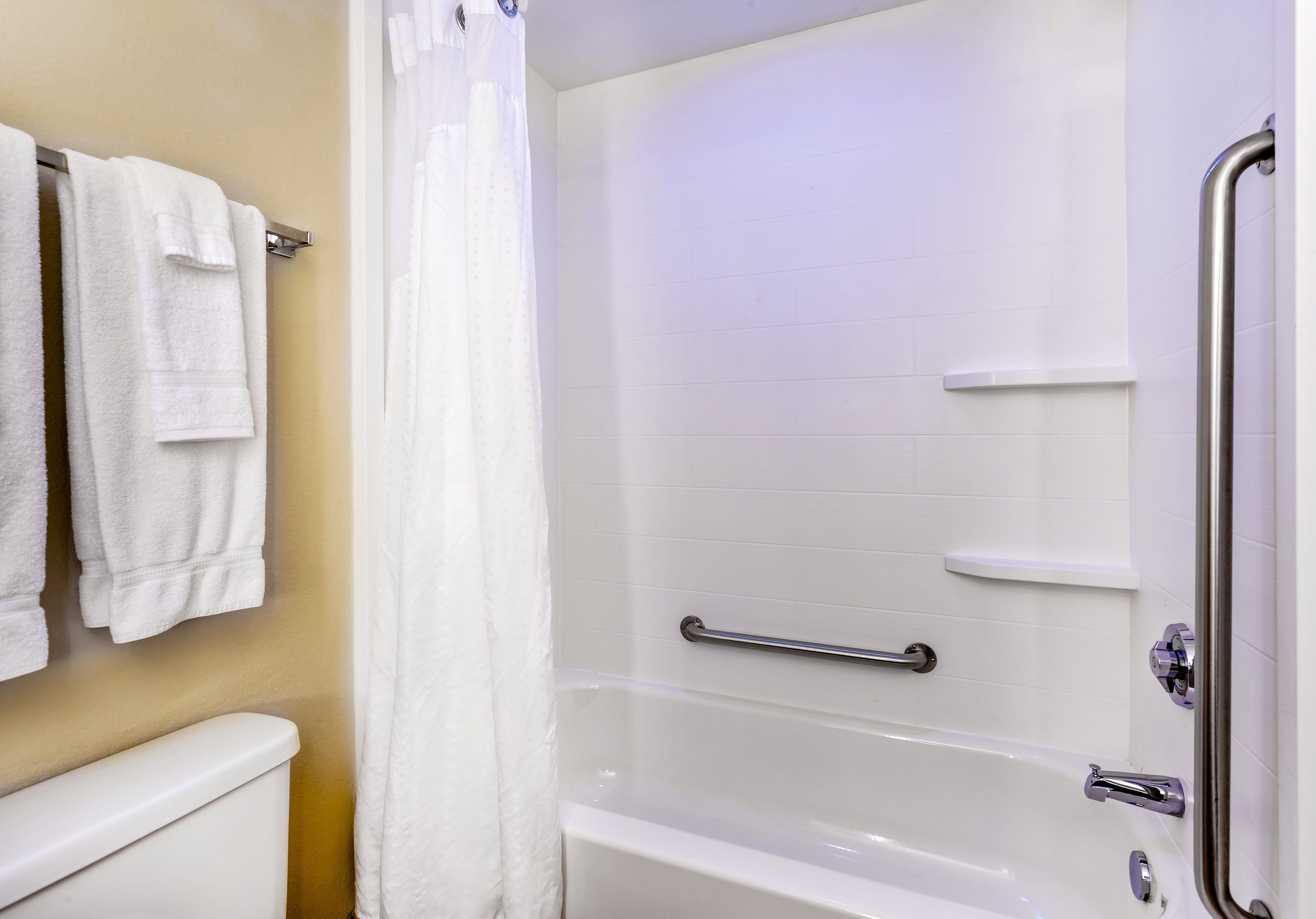 Un baño con una bañera blanca, una cortina de ducha, un asidero y un perchero con toallas.