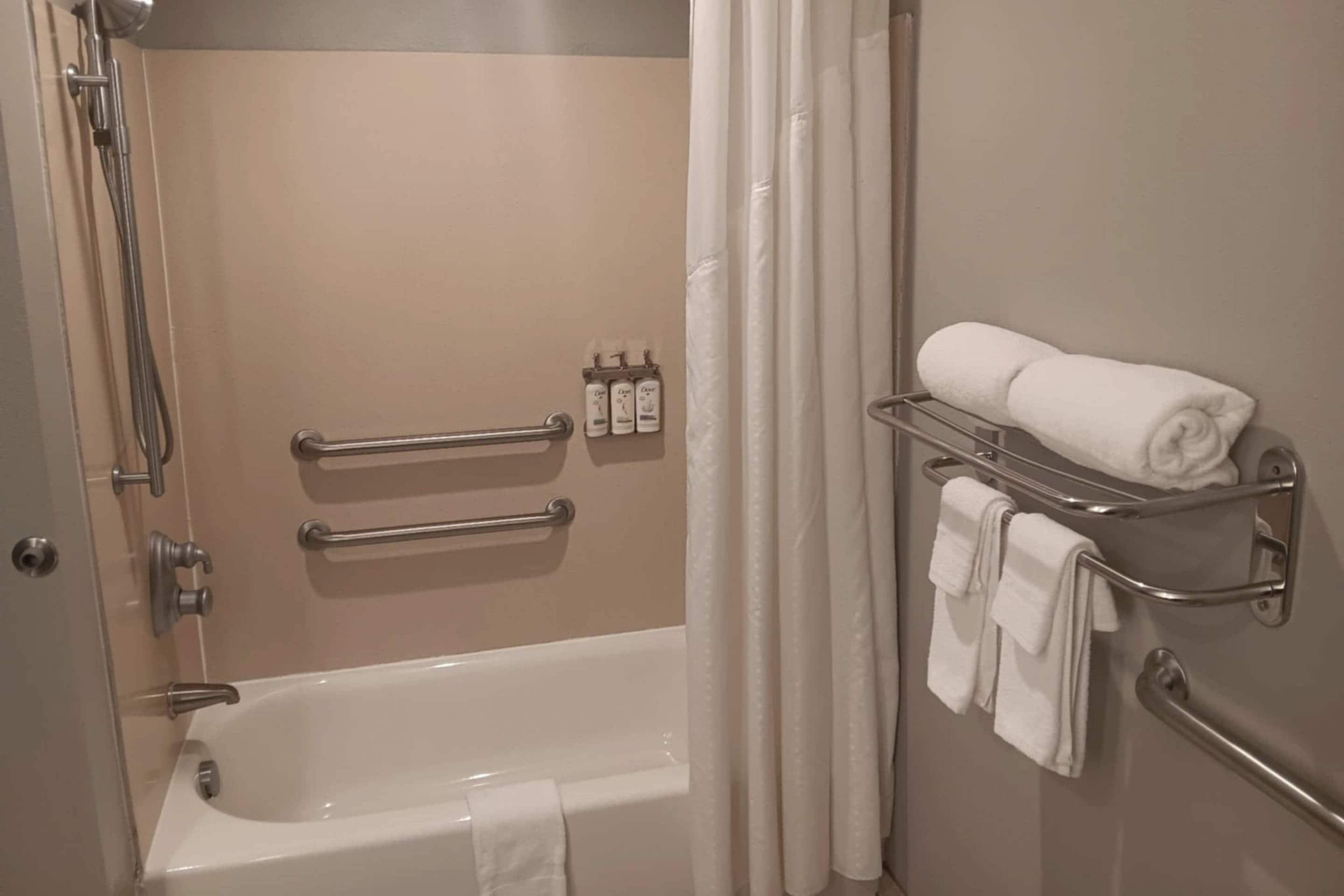 A bathroom with a bathtub, handrails, a towel rack, and a shower curtain.