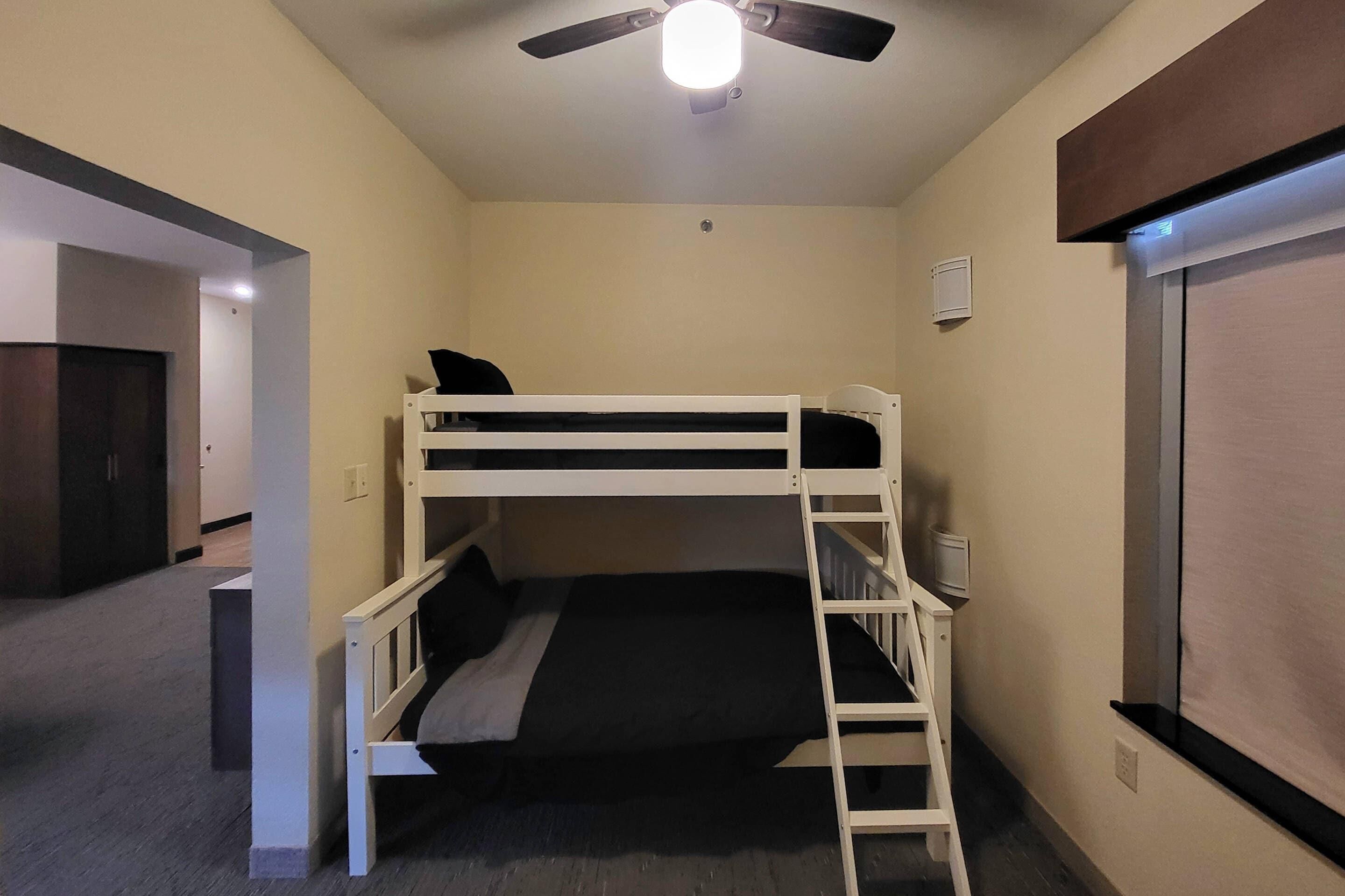 A bunk bed room with a ceiling fan, a window, and a door leading to another room.