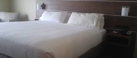 A hotel room with a large bed, a nightstand with a phone, and a wall-mounted lamp.