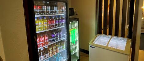 A vending machine with a Coca-Cola sign, a refrigerator, and a wooden partition in a room with wooden flooring.
