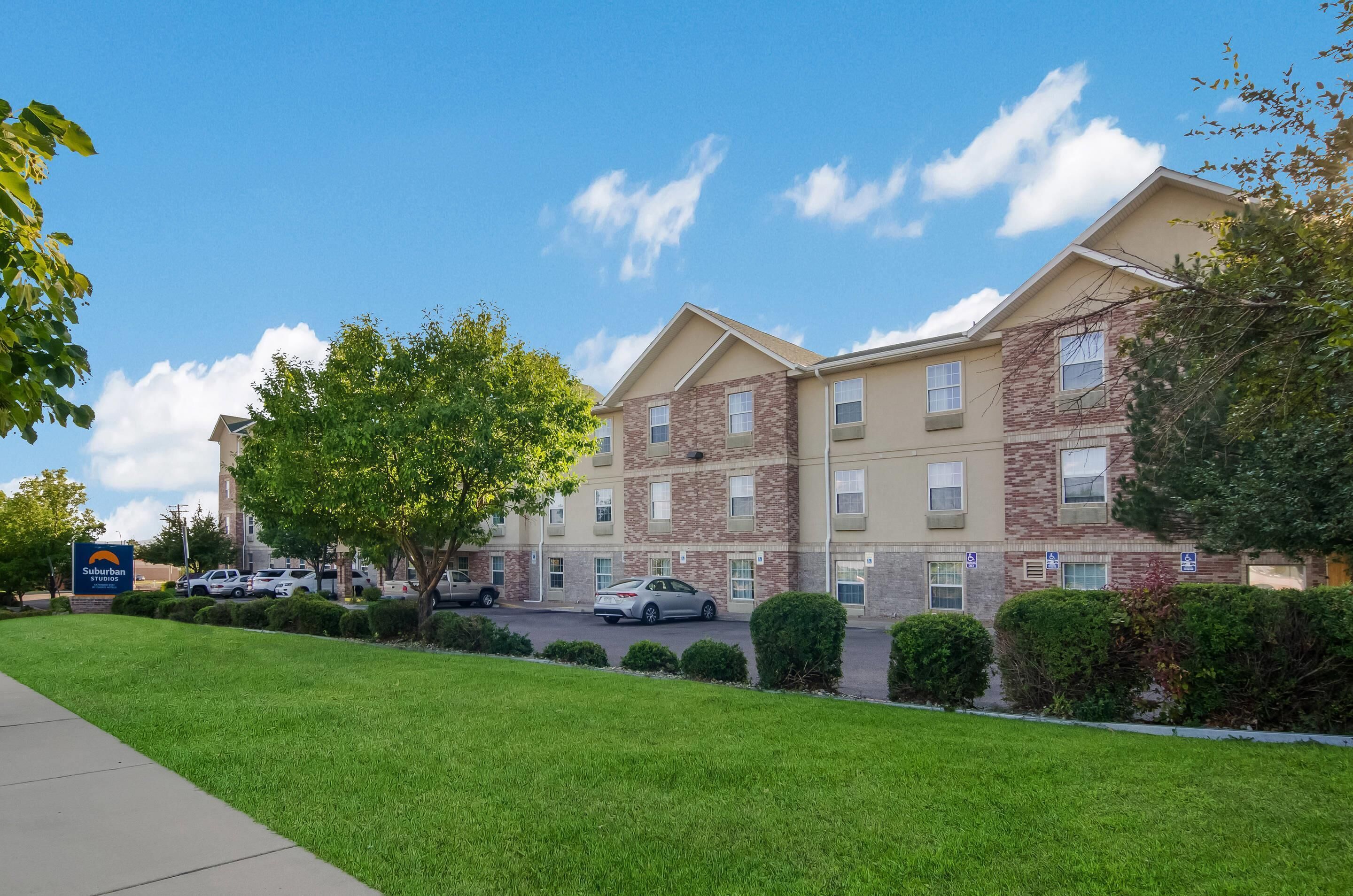 A multi-story hotel with a stone facade, a parking lot, and a well-maintained lawn.