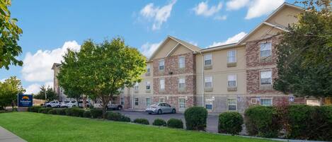 A multi-story hotel with a stone facade, a parking lot, and a well-maintained lawn.