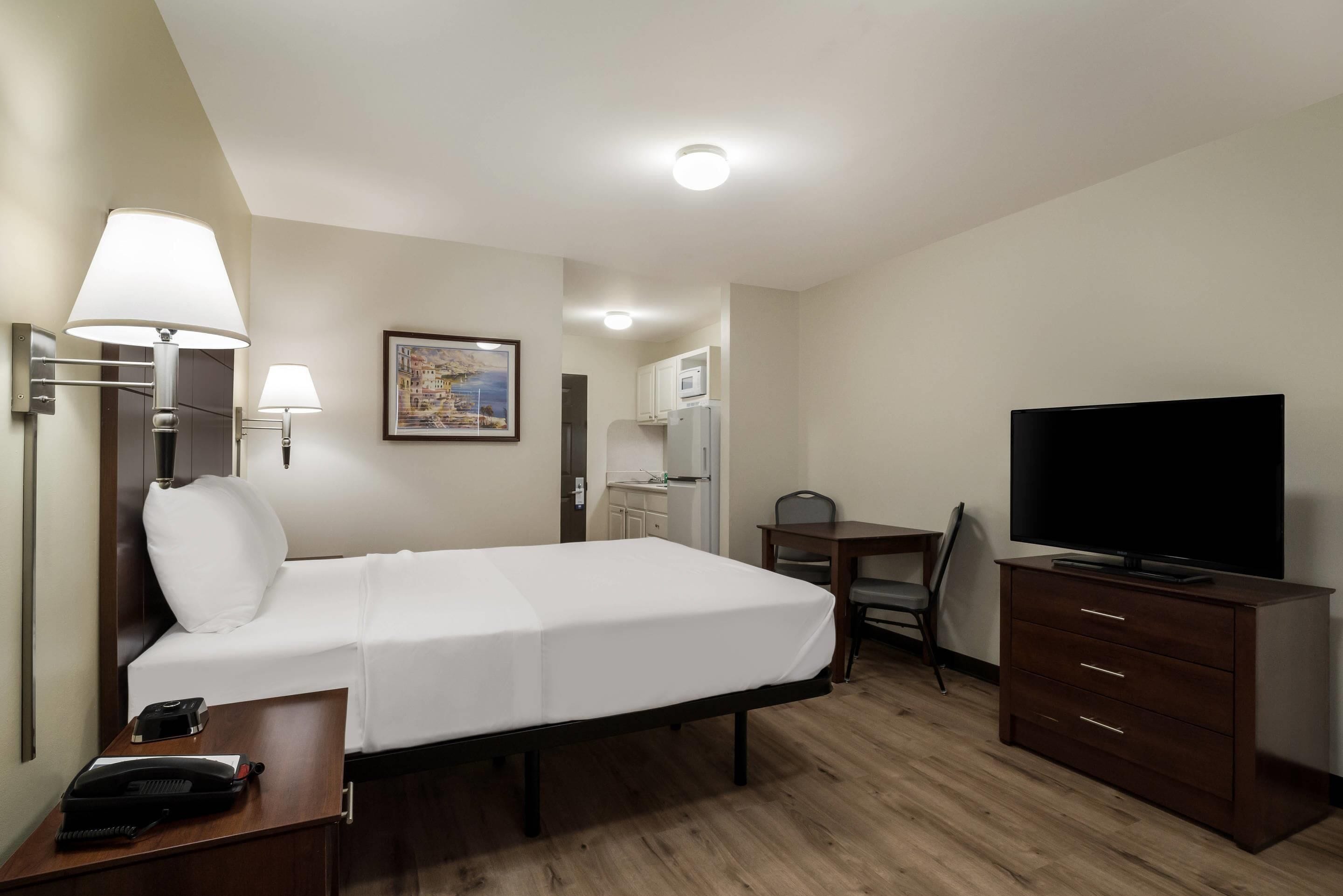 A hotel room with a bed, bedside lamps, a desk with a chair, a television, and a dresser.