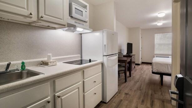 A compact kitchen with a microwave, refrigerator, and sink. There is a small dining area with a table and chairs. - Suburban Studios Denver Central-Arvada (Arvada)