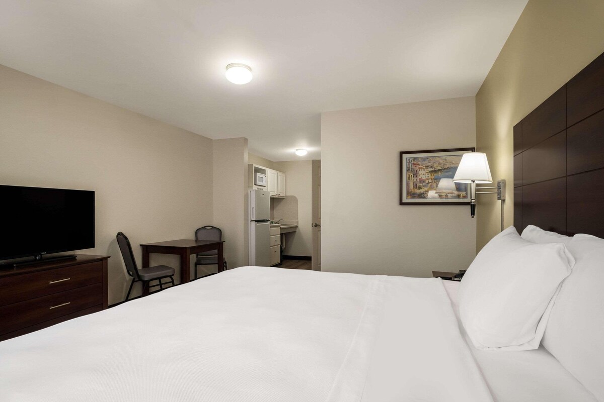 A hotel room with a bed, a desk, a chair, a television, a lamp, and a painting on the wall.