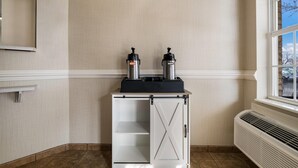 A corner room with a white cabinet, two coffee makers, a window, and a radiator. - Suburban Studios Denver Central-Arvada (Arvada)