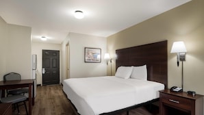 A hotel room with a large bed, bedside lamps, a desk, and a chair. - Suburban Studios Denver Central-Arvada (Arvada)