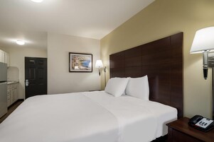 Habitación de hotel con una cama grande, una mesita de noche con una lámpara, un teléfono, un cuadro en la pared y una puerta que da al baño.