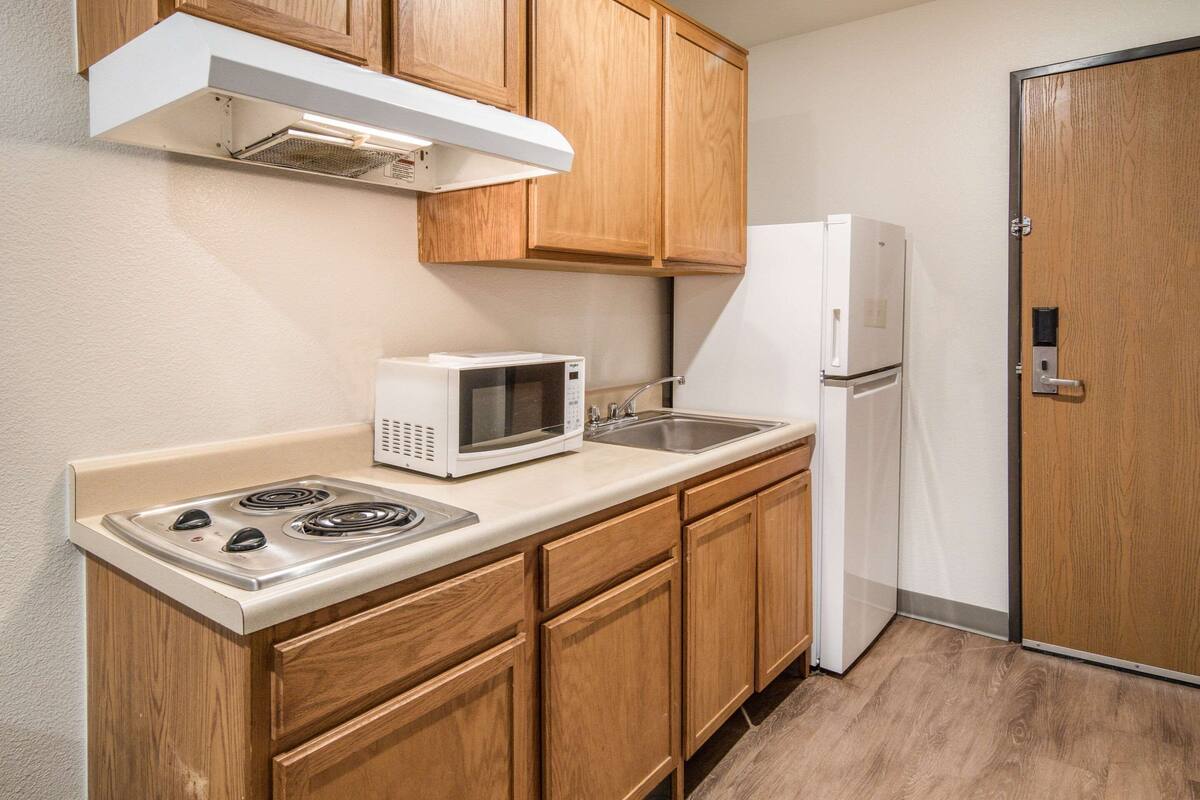 A compact kitchen with wooden cabinets, a microwave, a stove, a sink, and a refrigerator.
