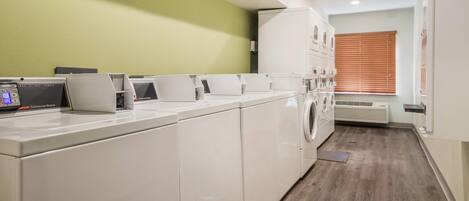 A laundry facility with multiple washing machines and dryers, a control panel, and a window with blinds.
