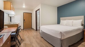 A hotel room with a bed, a desk with a chair, a wardrobe, and a door. - WoodSpring Suites Houston La Porte (La Porte)