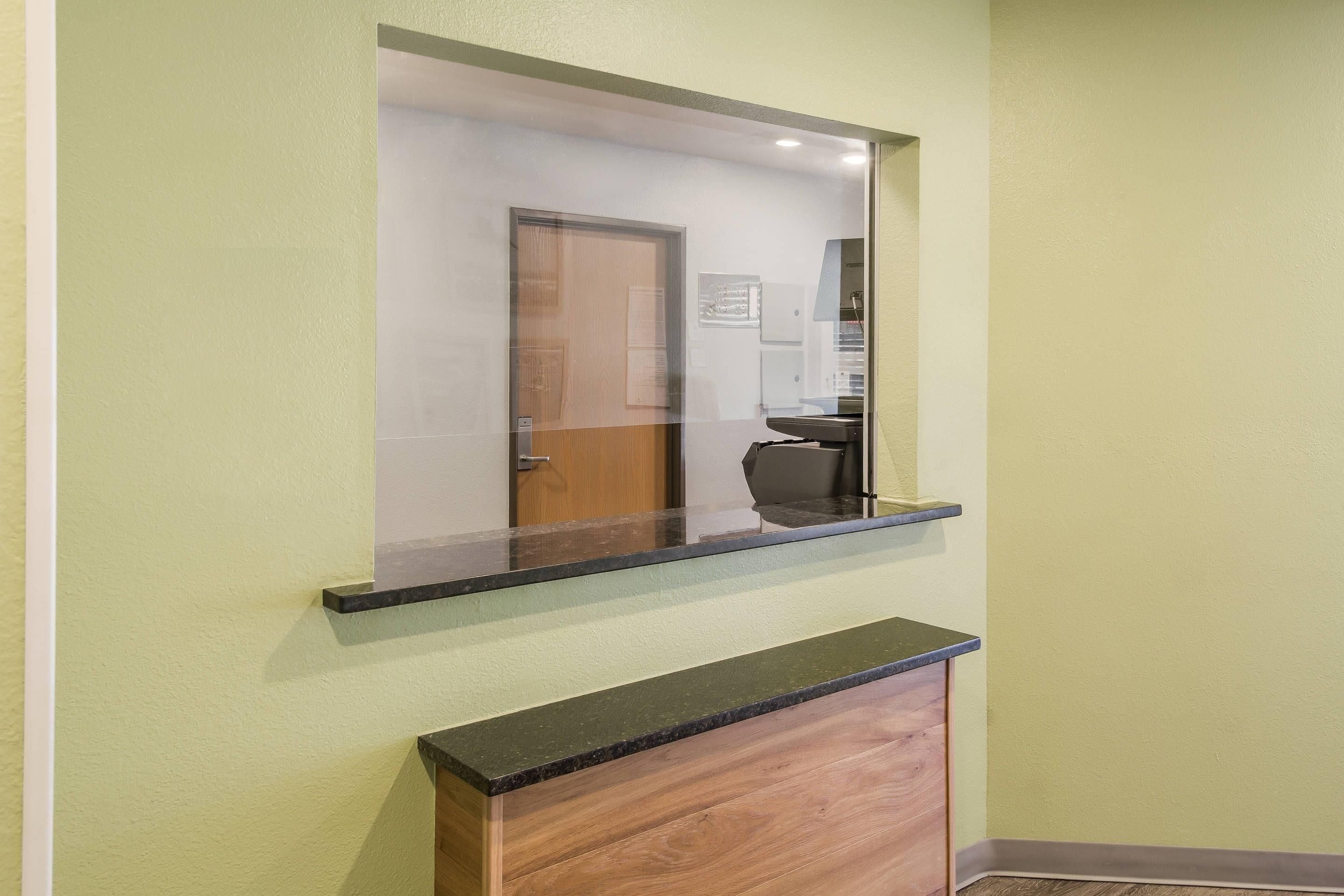 A hallway with a mirror reflecting a door and a desk.