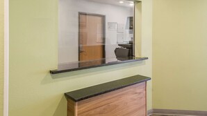 A reception desk with a glass partition and a wooden cabinet below. - WoodSpring Suites Houston La Porte (La Porte)
