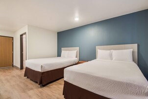 A hotel room with two beds, a wooden floor, and a blue accent wall.