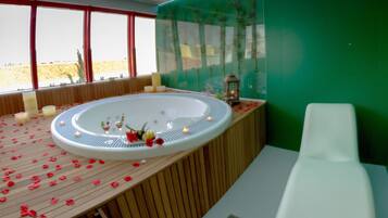 Relax in a serene spa area with a large hot tub, surrounded by candles and flowers.