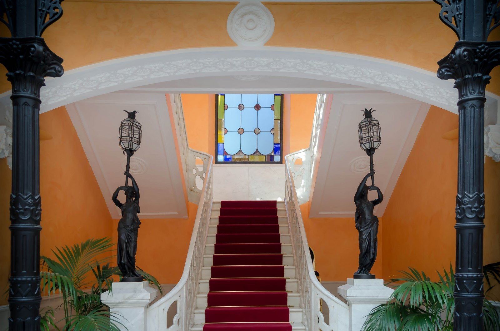 A grand staircase with red carpet, ornate black statues, and a stained glass window at the top.