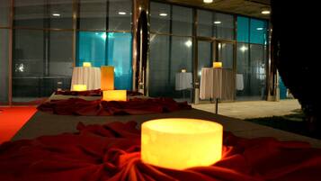 Una habitación con alfombra roja, mesas con velas y ventanas amplias.