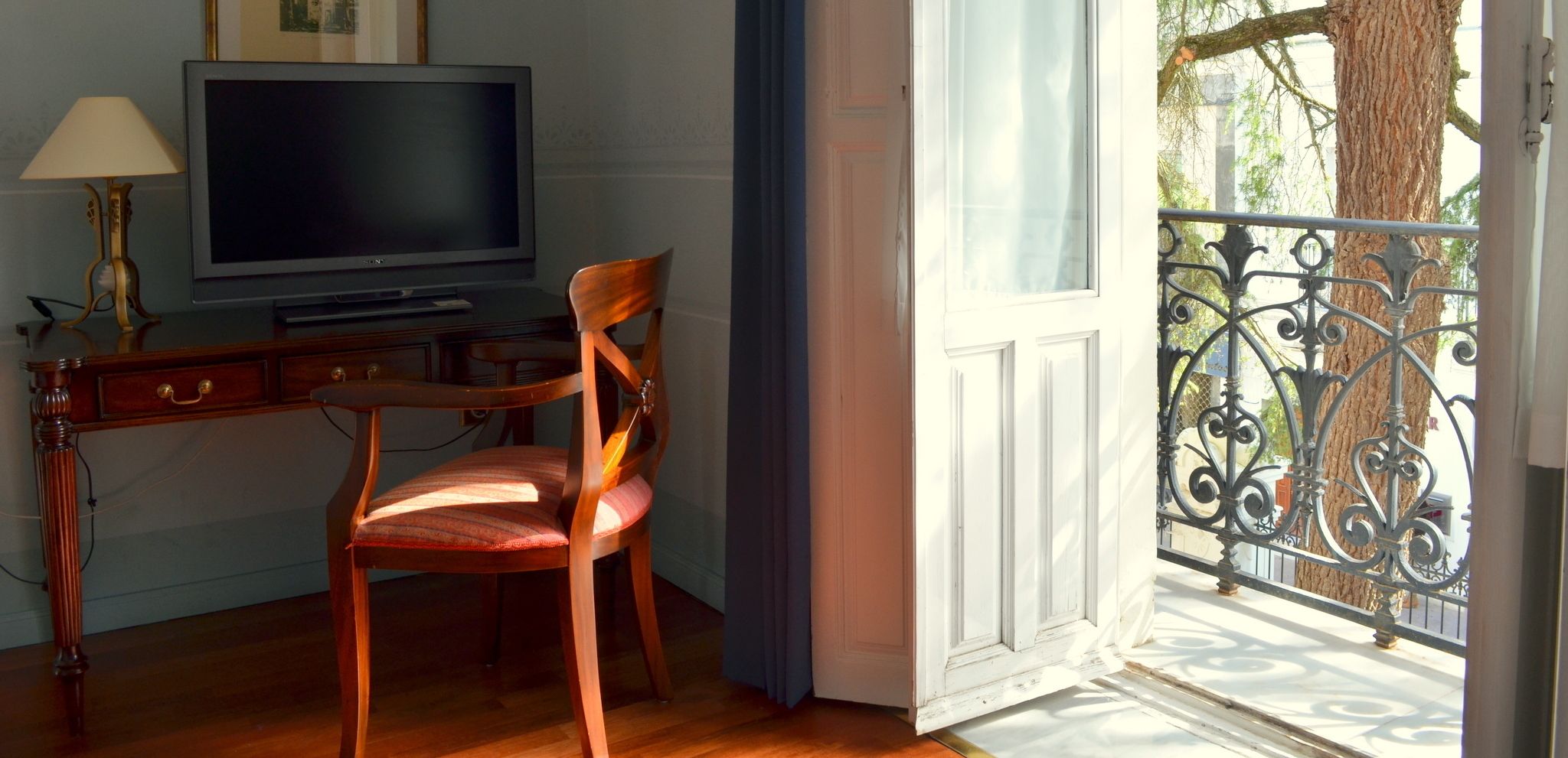 Een kamer met een houten bureau, een stoel, een televisie en een balkon met een sierhekwerk.