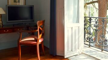Een kamer met een houten bureau, een stoel, een televisie en een balkon met een sierhekwerk.