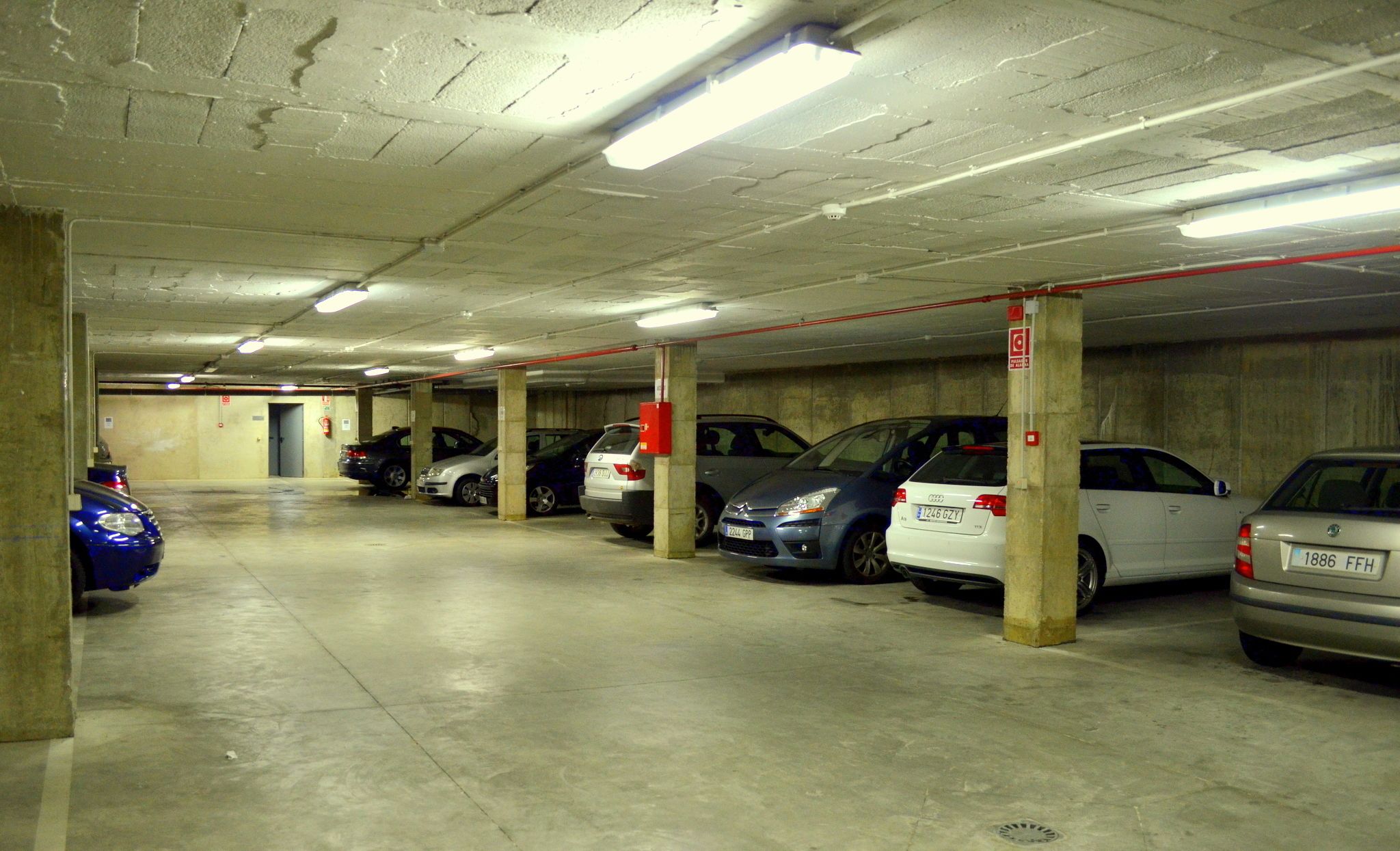 Un aparcamiento de varios niveles con pilares de hormigón e iluminación en el techo.