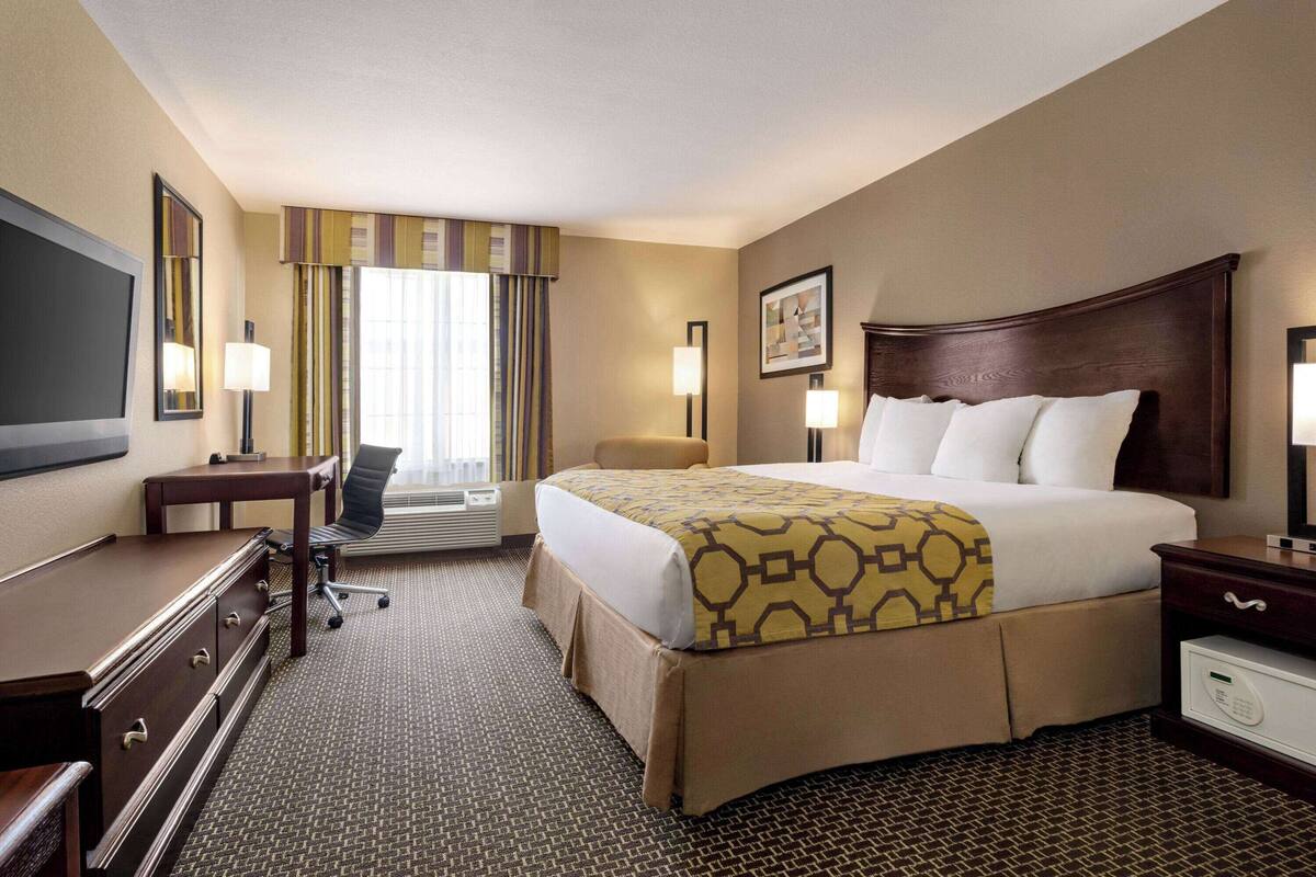 Habitación de hotel con una cama grande, un escritorio, una silla, un televisor de pantalla plana y una ventana con cortinas.