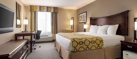 A hotel room with a large bed, a desk, a chair, a flat-screen TV, and a window with curtains.