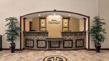 A reception area with a Baymont Inn & Suites sign, a stone reception desk, and two potted plants.