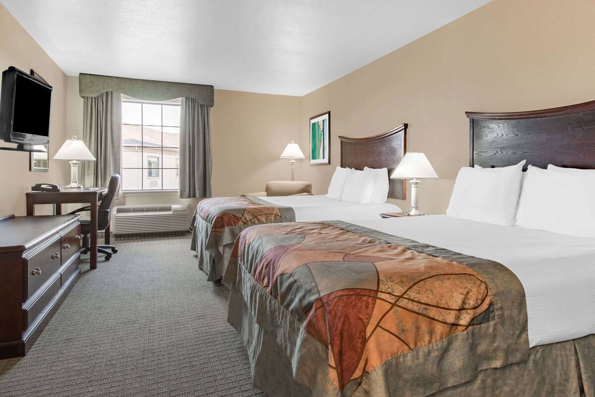 Habitación de hotel con cama, dos mesitas de noche, escritorio, silla, televisor y ventana con cortinas.
