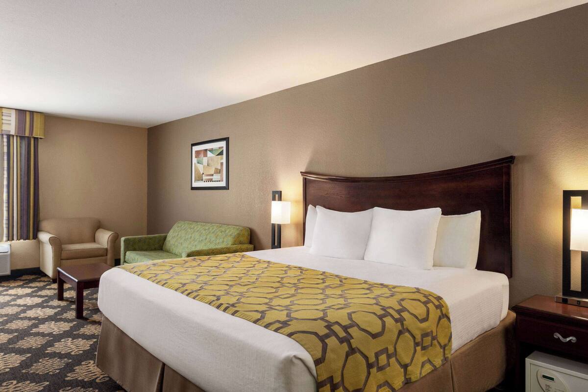 Habitación de hotel con una cama grande, una silla, una mesita, una lámpara y un cuadro en la pared.