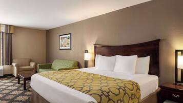Habitación de hotel con una cama grande, una silla, una mesita, una lámpara y un cuadro en la pared.
