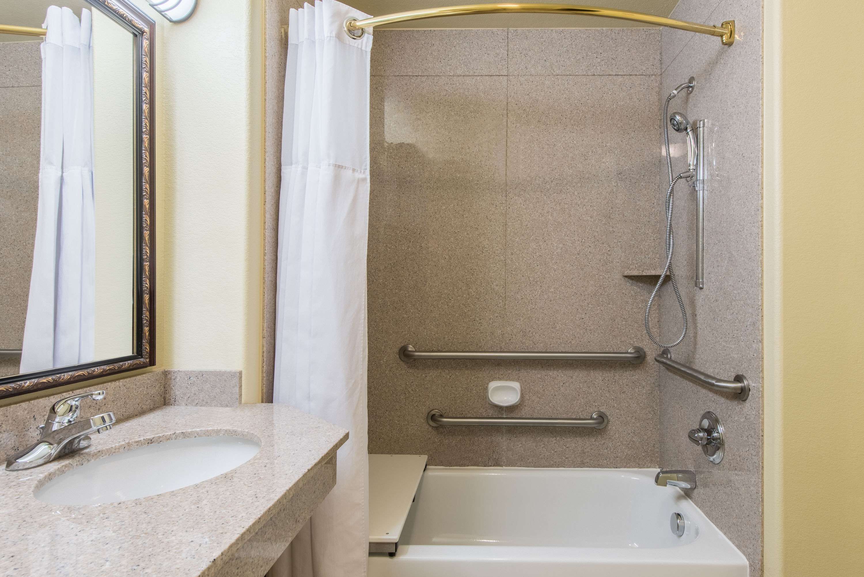 A bathroom with a sink, mirror, shower with grab bars, and a bathtub.